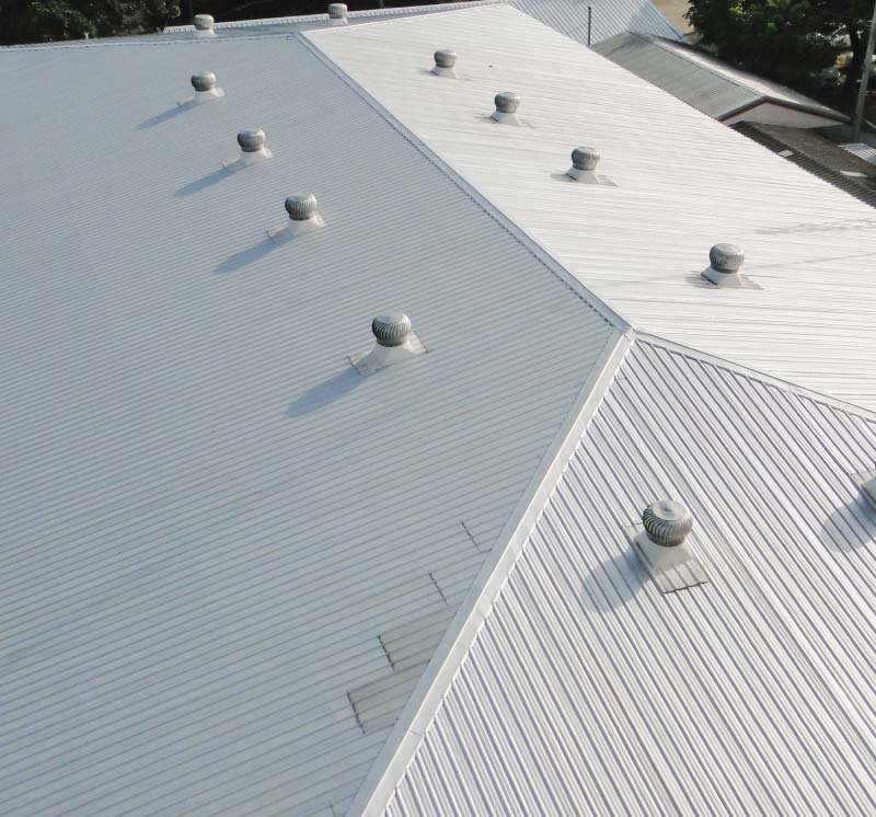 High-angle view of a large-scale commercial roofing project featuring a white, corrugated metal roof system with multiple industrial ventilation turbines installed by Rainforcing Roofing.