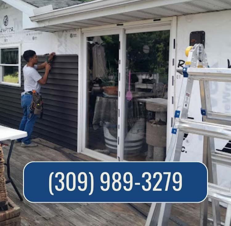 A professional installer from Rainforcing Roofing & Exteriors carefully applying dark gray horizontal vinyl siding over protective house wrap on a residential property. The company logo and contact number, (309) 989-3279, are prominently displayed as part of the service advertisement.