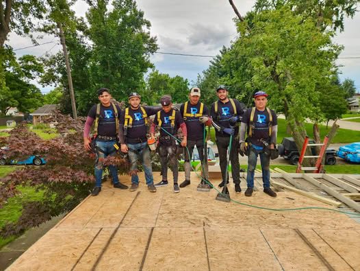 The Rainforcing Roofing expert team stands on a residential roof deck during a restoration project. Every team member is wearing a professional branded company shirt and safety harness, demonstrating our commitment to quality and job site safety.